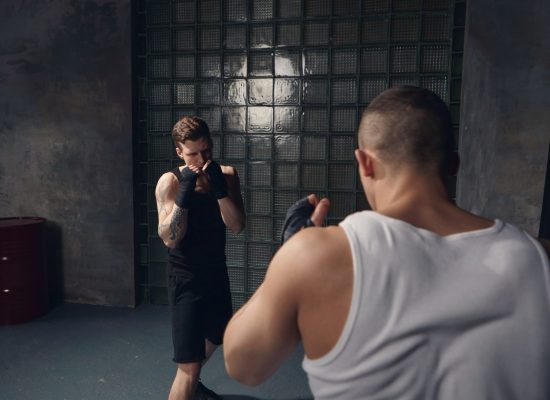 Back view of unrecognizable male fighter with broad muscular shoulders fighting against young Caucasian guy with tattoos wearing black outfit and bandages. Sports, martial arts and competition